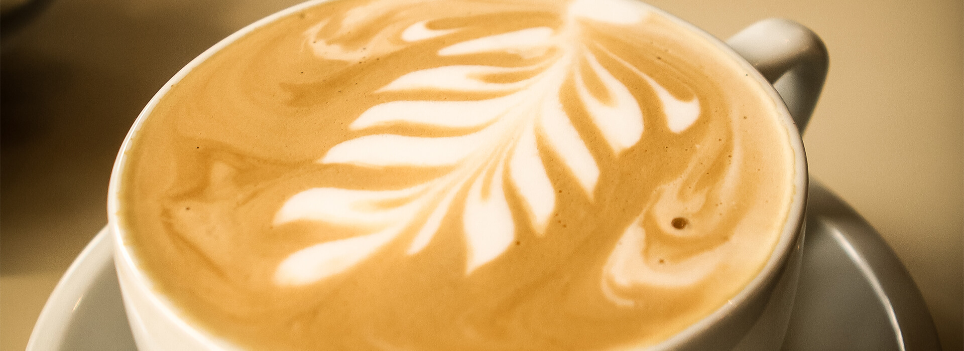 A beautifully decorated cup of coffee with a foam leaf.