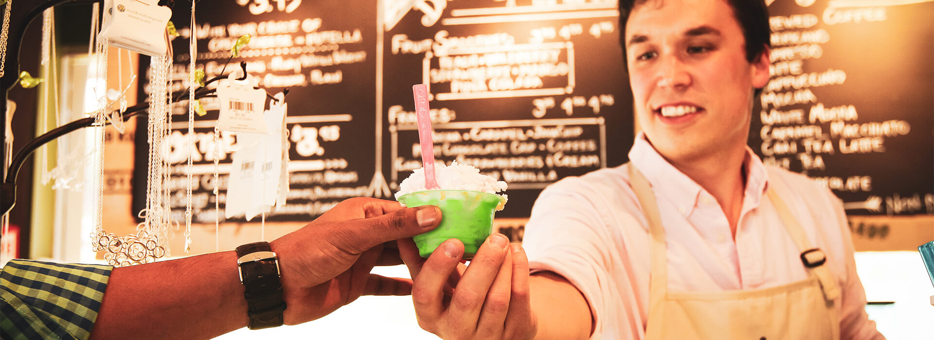 A male barista serving a gelato to a customer at the Grapes and Grind counter.